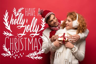 Kış kıyafetli mutlu çift Noel hediyelerini kırmızıda tutuyorlar ve kutsal bir Noel çizimi yapıyorlar.