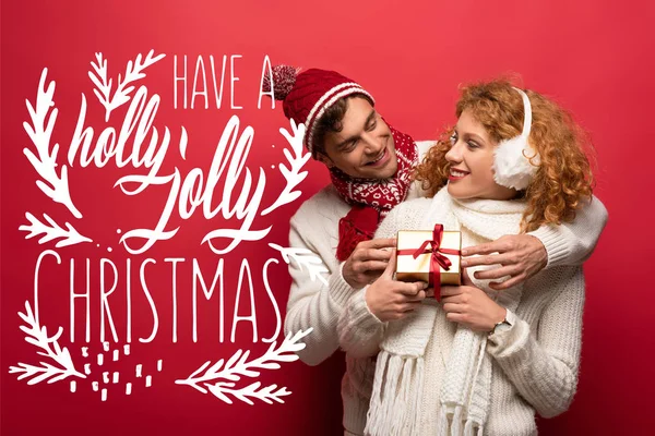 Kış kıyafetli mutlu çift Noel hediyelerini kırmızıda tutuyorlar ve kutsal bir Noel çizimi yapıyorlar.