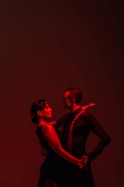 sensual couple of dancers performing tango on dark background with red illumination clipart