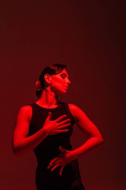 Siyah elbiseli şehvetli dansçı kırmızı ışıkla karanlık arka planda tango yapıyor.