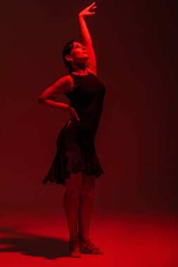 Siyah elbiseli zarif bir dansçı koyu arkaplanda kırmızı ışıkla tango yapıyor.