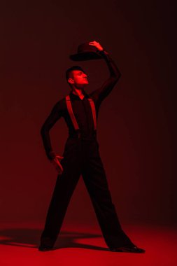 Kırmızı ışıkla arka planda tango yaparken şapkasını başının üstünde tutan şık bir dansçı.