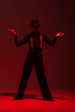 Siyah elbiseli ve şapkalı şık dansçı koyu arkaplanda kırmızı ışıkla tango yapıyor.