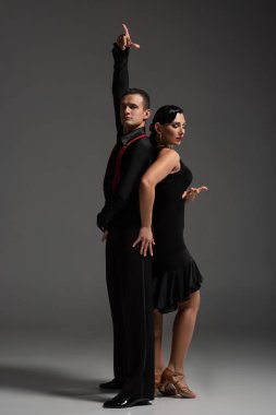 Gri arka planda tango yapan siyah elbiseli iki zarif dansçı.