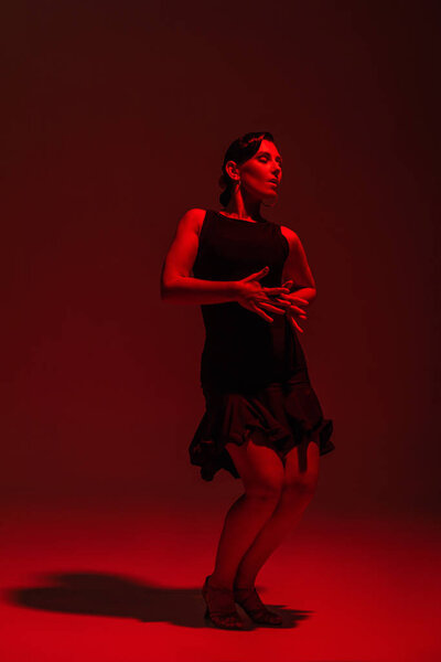 passionate dancer in black dress performing tango on dark background with red lighting