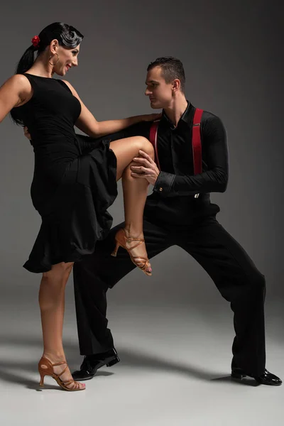 灰色の背景でタンゴを踊りながらパートナーの脚に触れる官能的なダンサー — ストック写真