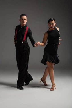 Gri arka planda tango yaparken kameraya bakan şık dansçılar.