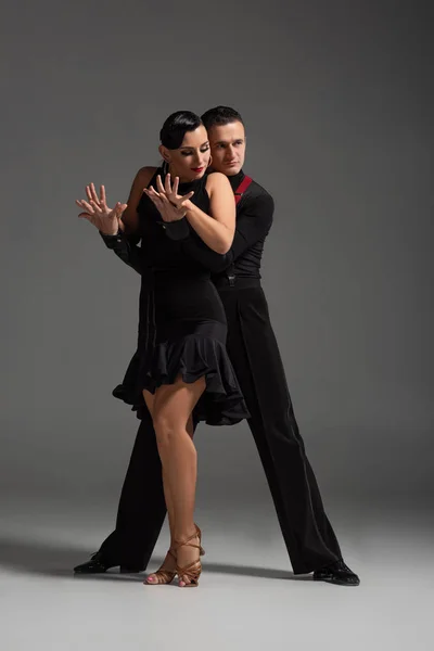 Elegante Casal Dançarinos Roupas Pretas Realizando Tango Fundo Cinza — Fotografia de Stock