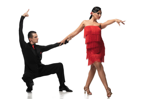 elegant dancer squatting and holding hand of attractive partner while performing tango on white background