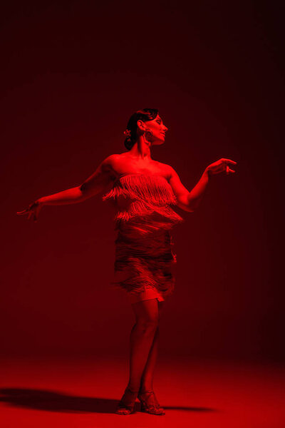beautiful dancer in dress with fringe performing tango on dark background with red illumination