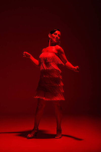 smiling, elegant dancer performing tango on dark background with red illumination