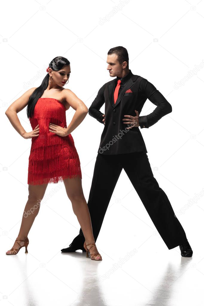 stylish couple of dancers holding hands on hips while performing tango on white background