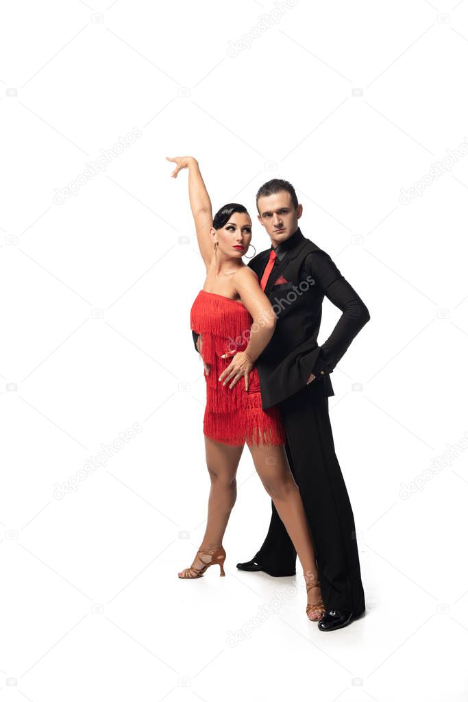 handsome, stylish dancer looking at camera while performing tango with attractive partner on white background