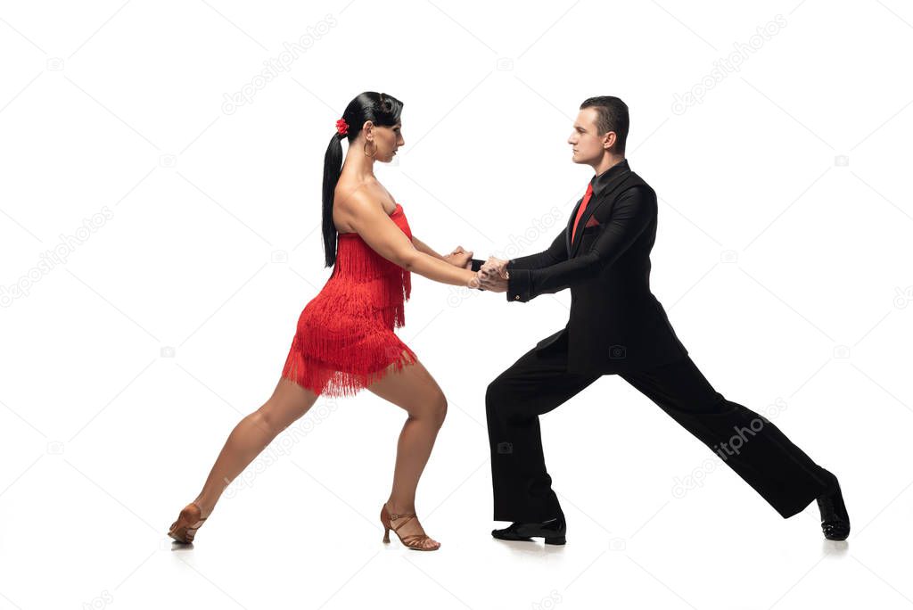 side view of elegant dancers holding hands and looking at each other while performing tango on white background