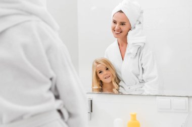 Mutlu anne ve tatlı kızın seçici odağı banyoda aynaya bakıyor. 
