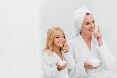 Neşeli anne ve kız banyoda kozmetik krem sürüyor. 
