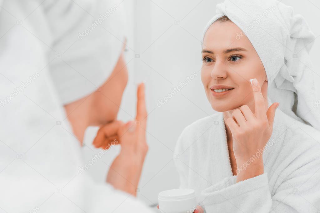 Selective focus of woman applying cosmetic cream in bathroom 