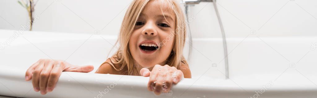 panoramic shot of happy child taking bath and laughing at home 