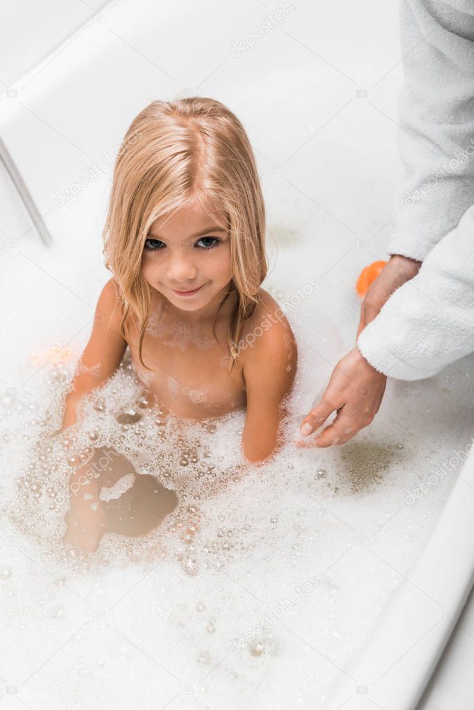 overhead view of cute child taking bath near mother 