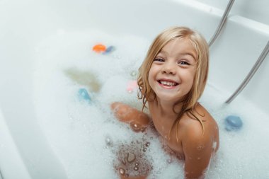 Mutlu çıplak çocuk evde banyo köpüğüyle banyo yapıyor. 