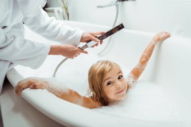 Sevimli ve çıplak çocuk banyoda annesinin yanında banyo yapıyor. 