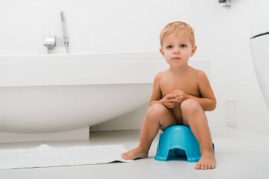 cute toddler boy sitting on blue potty near bathtub  clipart