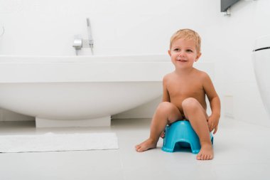 happy toddler boy sitting on blue potty near bathtub  clipart