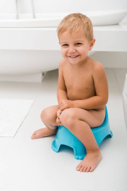 smiling toddler boy sitting on blue potty near bathtub  clipart