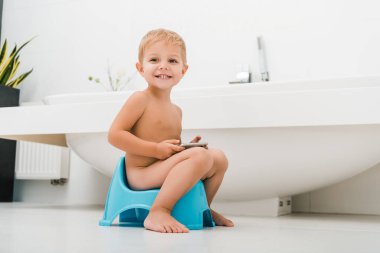 happy toddler boy sitting on potty and using smartphone  clipart