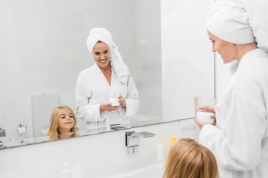 Güzel bir kızın yanında kozmetik kremi taşıyan mutlu bir annenin seçici odak noktası. 