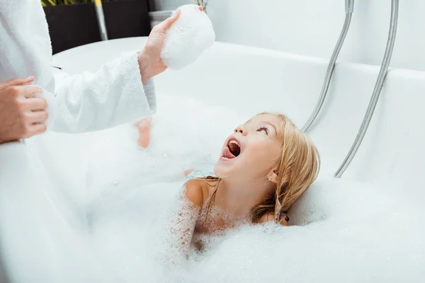 兴奋的孩子看着妈妈在浴室里用泡沫洗澡 — 图库照片