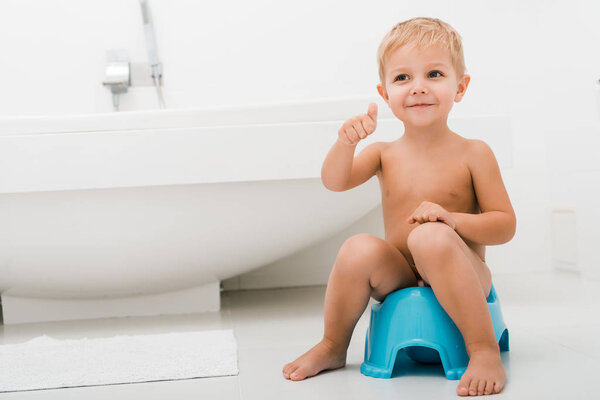 happy naked toddler boy gesturing while sitting on blue potty 