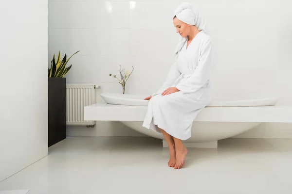 穿着白色浴衣的漂亮女人坐在现代浴室里 — 图库照片