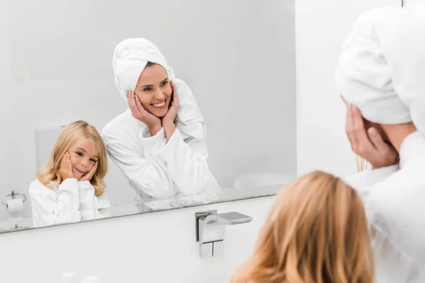 穿着浴衣的快乐妈妈和可爱女儿在浴室里触摸脸庞的选择性焦点 — 图库照片