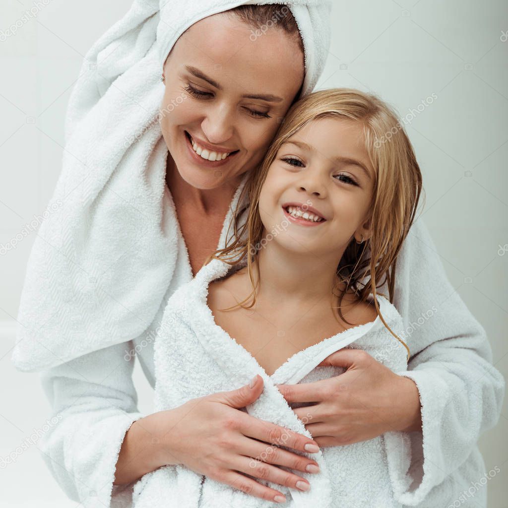 cheerful mother smiling while hugging daughter in bathroom 