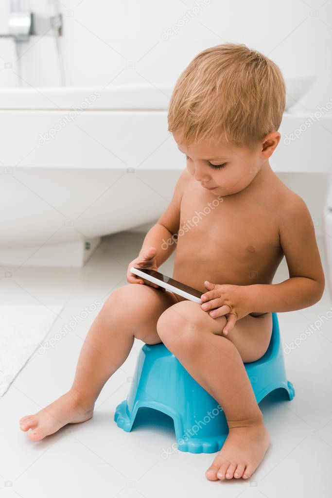 adorable toddler boy sitting on potty and using smartphone 