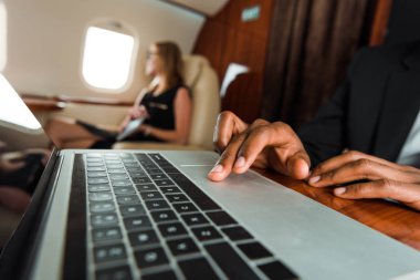 selective focus of african american businessman typing on laptop near businesswoman in plane  clipart