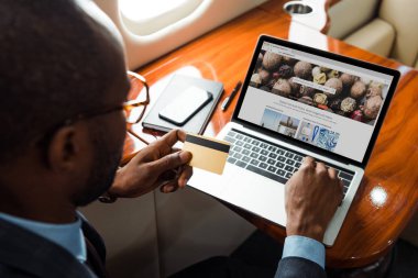 Seçici odak noktası Afrika kökenli Amerikalı iş adamı dizüstü bilgisayarın yanında özel uçağın fotoğraf web sitesi ile kredi kartı tutuyor. 