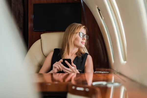 Selektywne Skupienie Atrakcyjnej Bizneswoman Okularach Posiadających Smartfon Prywatnym Odrzutowcu — Zdjęcie stockowe