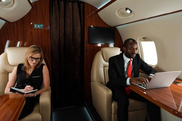 African American Businessman Using Laptop Businesswoman Writing Notebook Private Jet — Stock Photo, Image