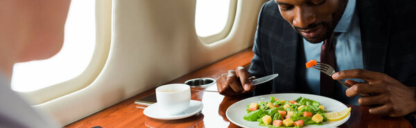 panoramic shot of african american businessman near tasty dish and businesswoman in private plane 