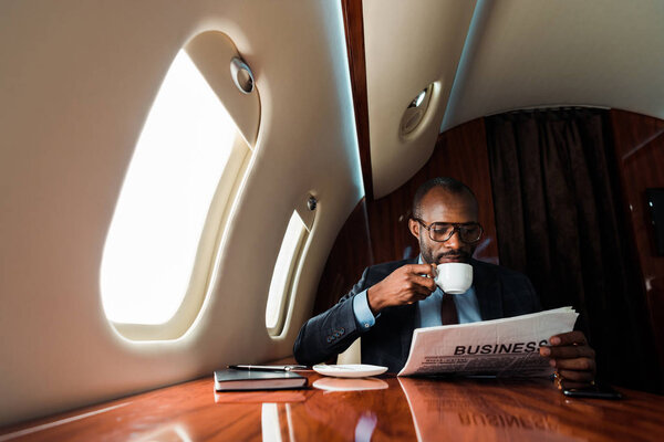 Африканский американский бизнесмен читает деловую газету, когда пьет кофе в частном самолете
 