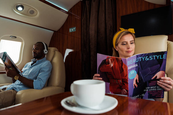 selective focus of woman and african american man reading magazines in plane 