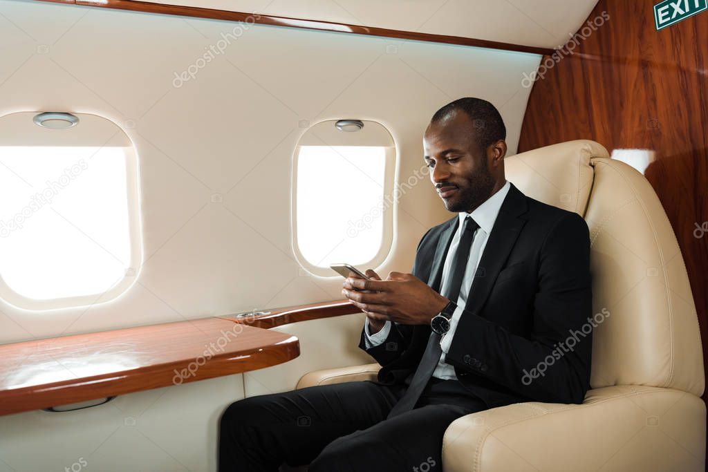 handsome african american businessman using smartphone in private jet 