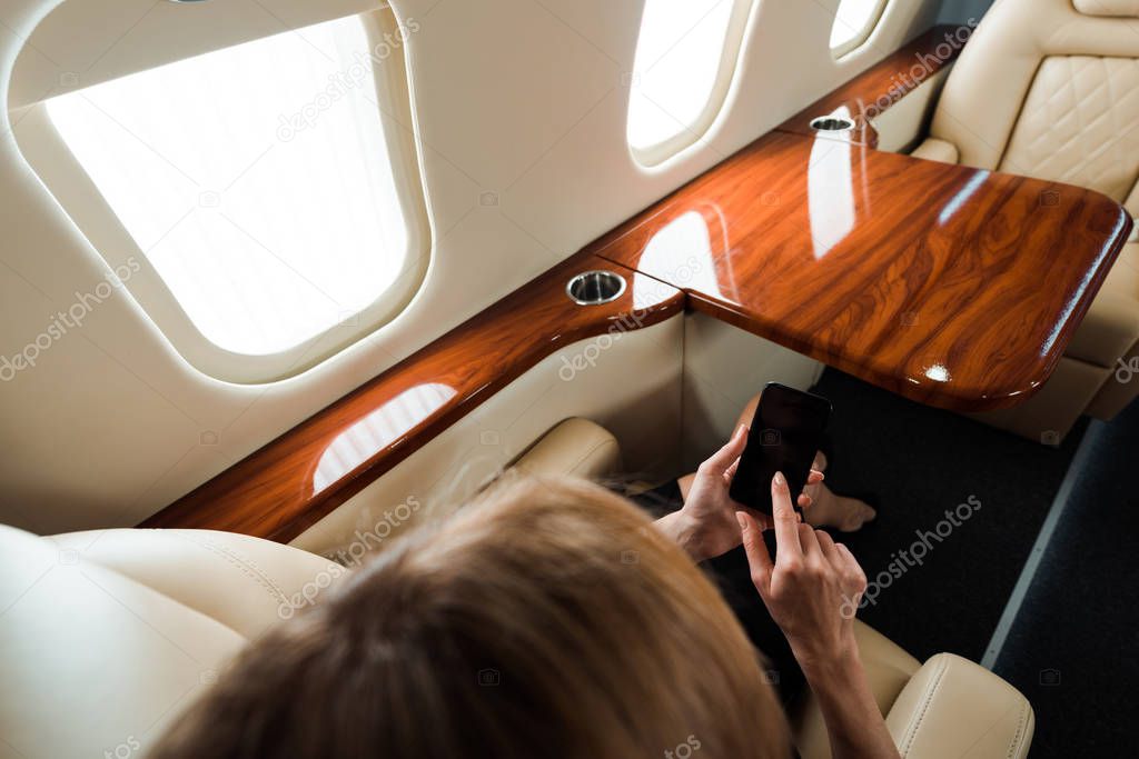 top view of businesswoman holding smartphone with blank screen in private jet 