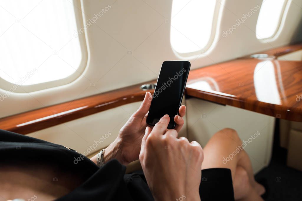 cropped view of businesswoman holding smartphone with blank screen in private jet