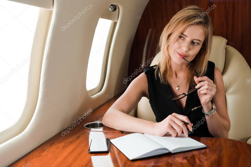 selective focus of pensive businesswoman holding pen and glasses near notebook 