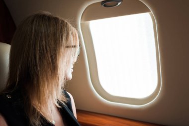 Gözlüklü bir iş kadını uçak camına bakıyor. 