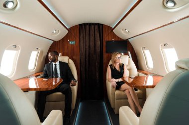 Yakışıklı Afro-Amerikan iş adamı ve özel uçakta oturan çekici iş kadınının seçici odağı 