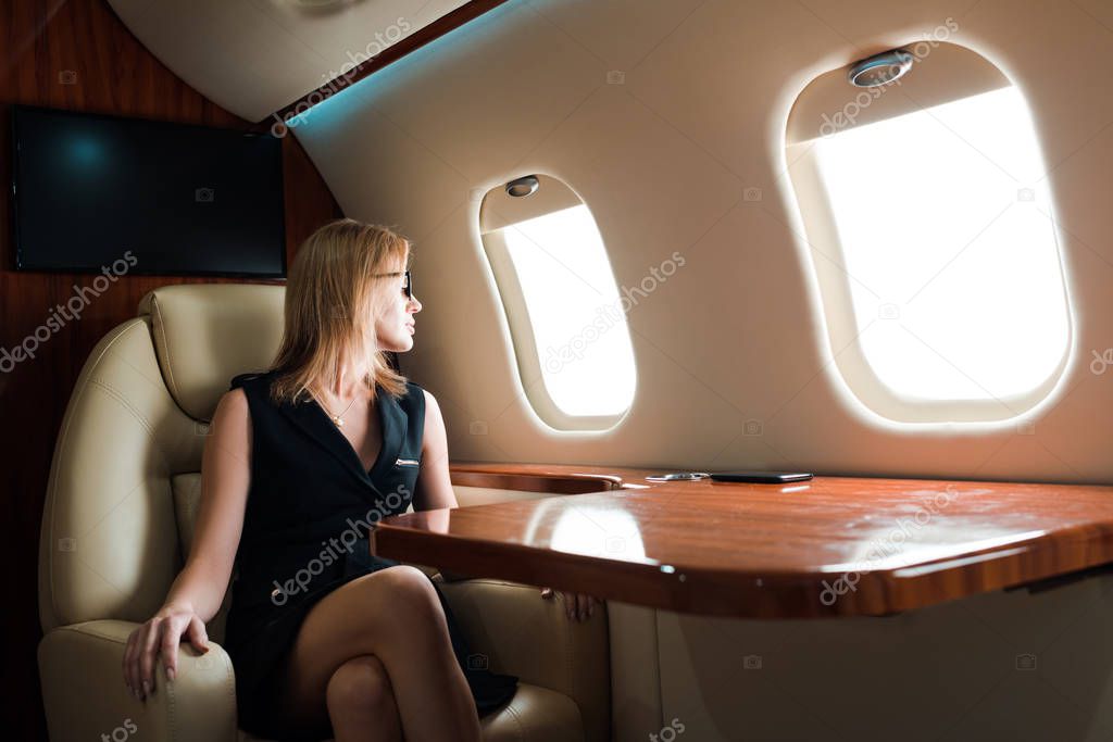attractive businesswoman in glasses looking at airplane window in private jet 
